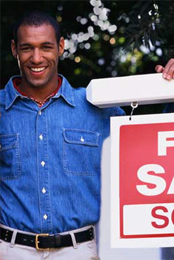 A smiling couple standing next to a 'For Sale: Sold' sign.